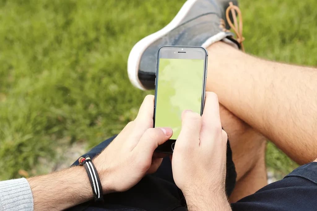 Zwei Hände halten ein Smartphone, im Hintergrund Rasen
